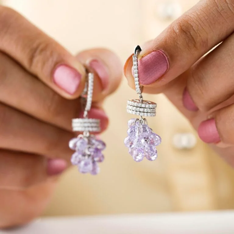 Close-up of hands holding elegant diamond and gemstone earrings with delicate lavender gemstones.